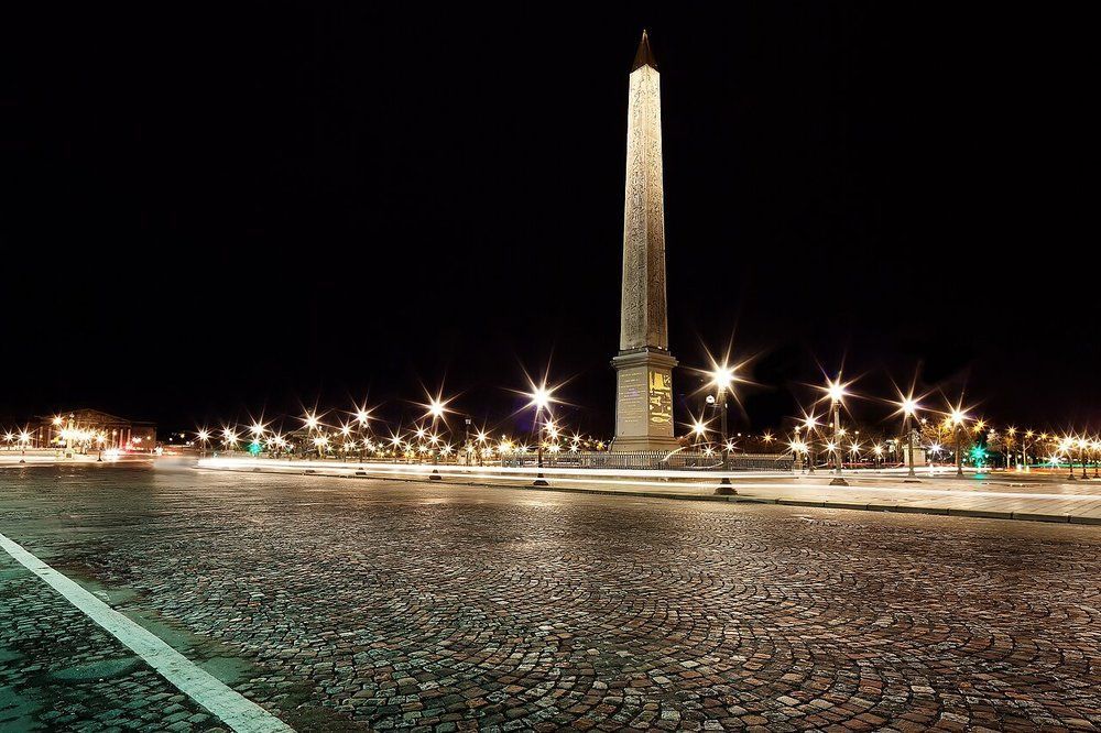 The Place de la Concorde at night, the floodlit obelisk surrounded by starburst street lamps, wet cobbles in the foreground