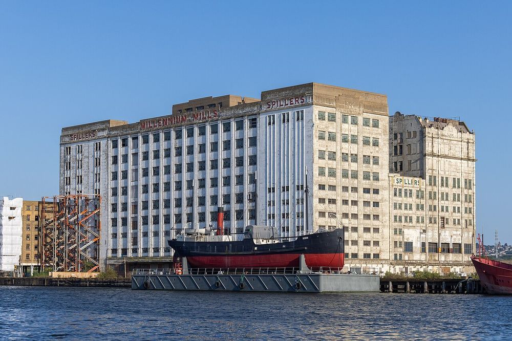 Millennium Mills on the Royal Victoria Dock in London. A white facade lettered SPILLERS MILLENNIUM MILLS in red, with a black steamship moored in front