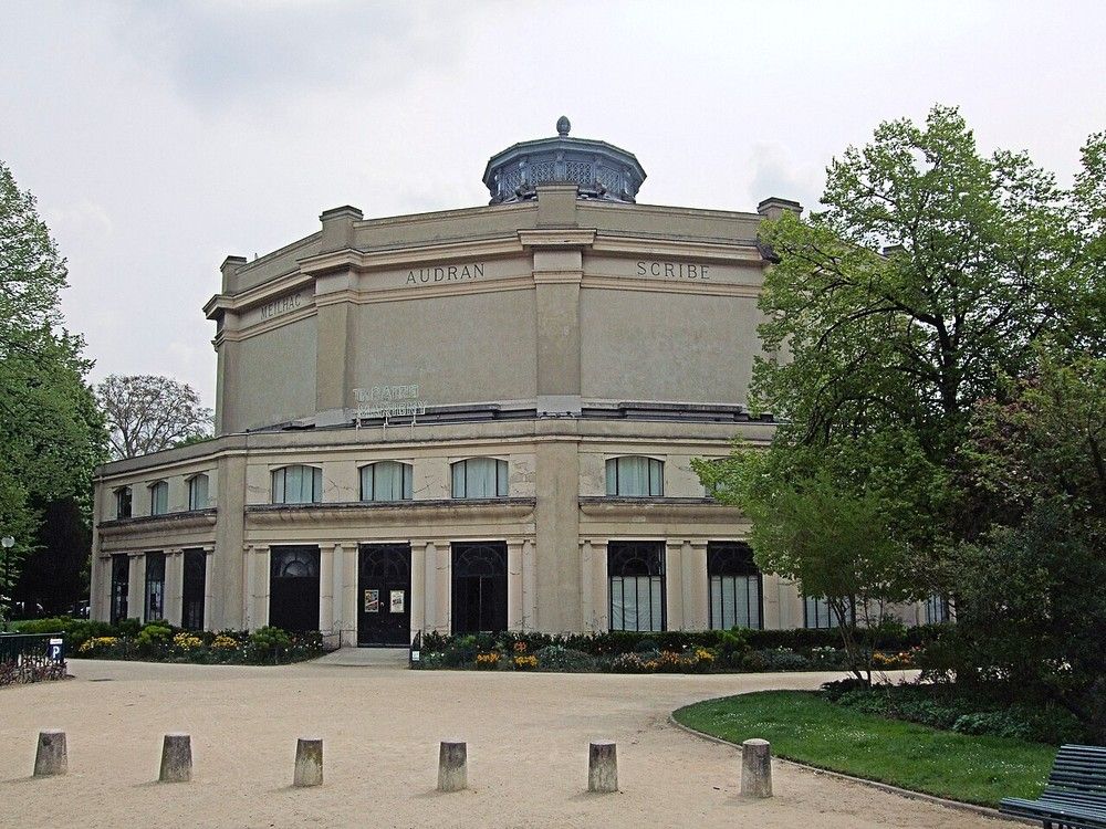 The Théâtre Marigny in the gardens off the Champs-Élysées in Paris. The names MEILHAC, AUDRAN and SCRIBE are carved into its round wall, and a row of low stone bollards stands in the forecourt
